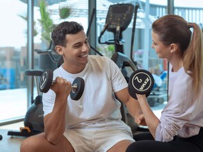 Un gimnasio con equipo de ejercicio y una persona sentada en un banco.