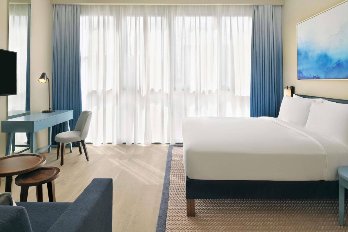 Une chambre d’hôtel avec un lit, un bureau, une chaise, une télévision et un tableau au mur.