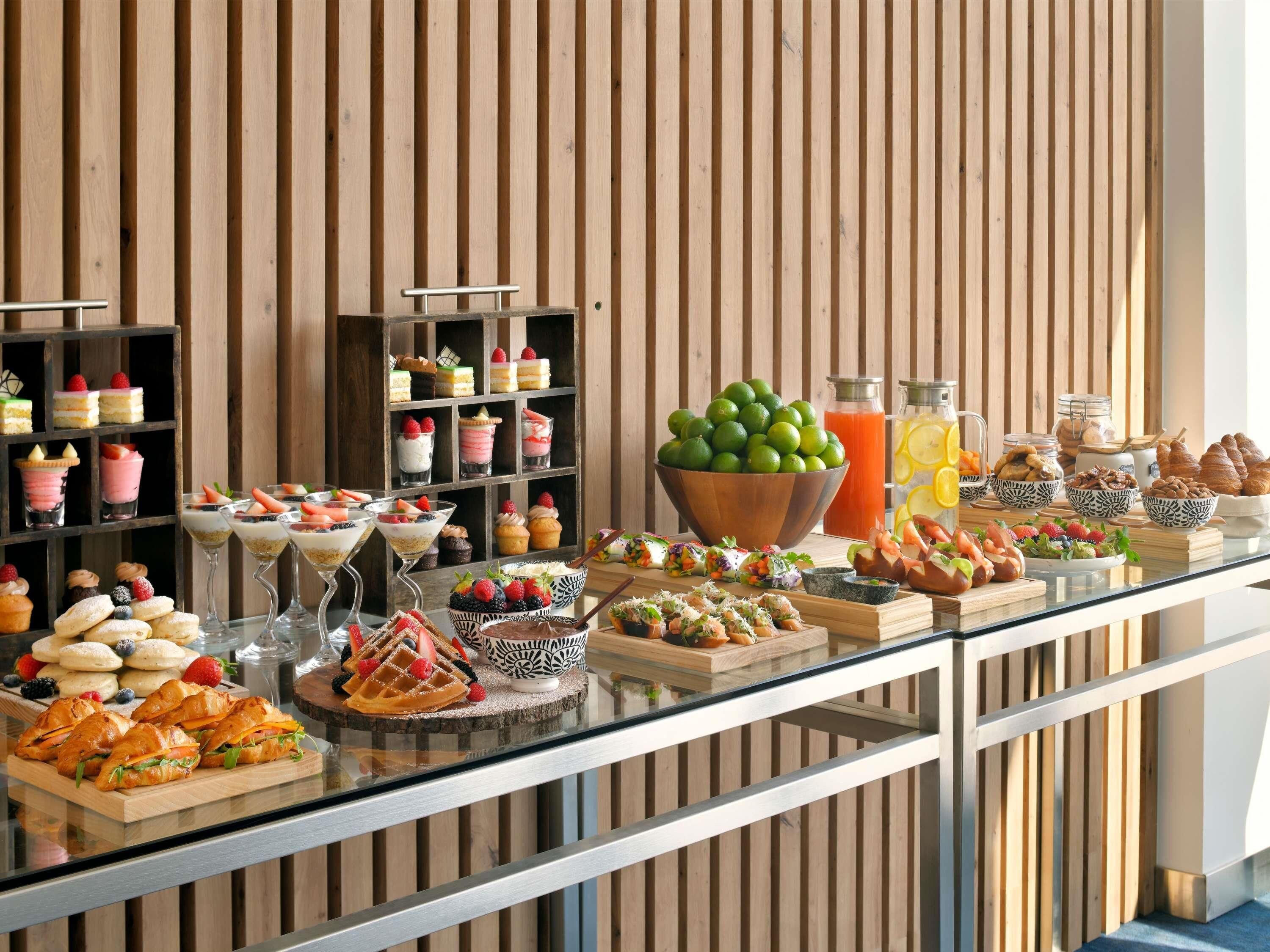Monipuolinen buffet, jossa on tarjolla erilaisia jälkiruokia, hedelmiä ja juomia.