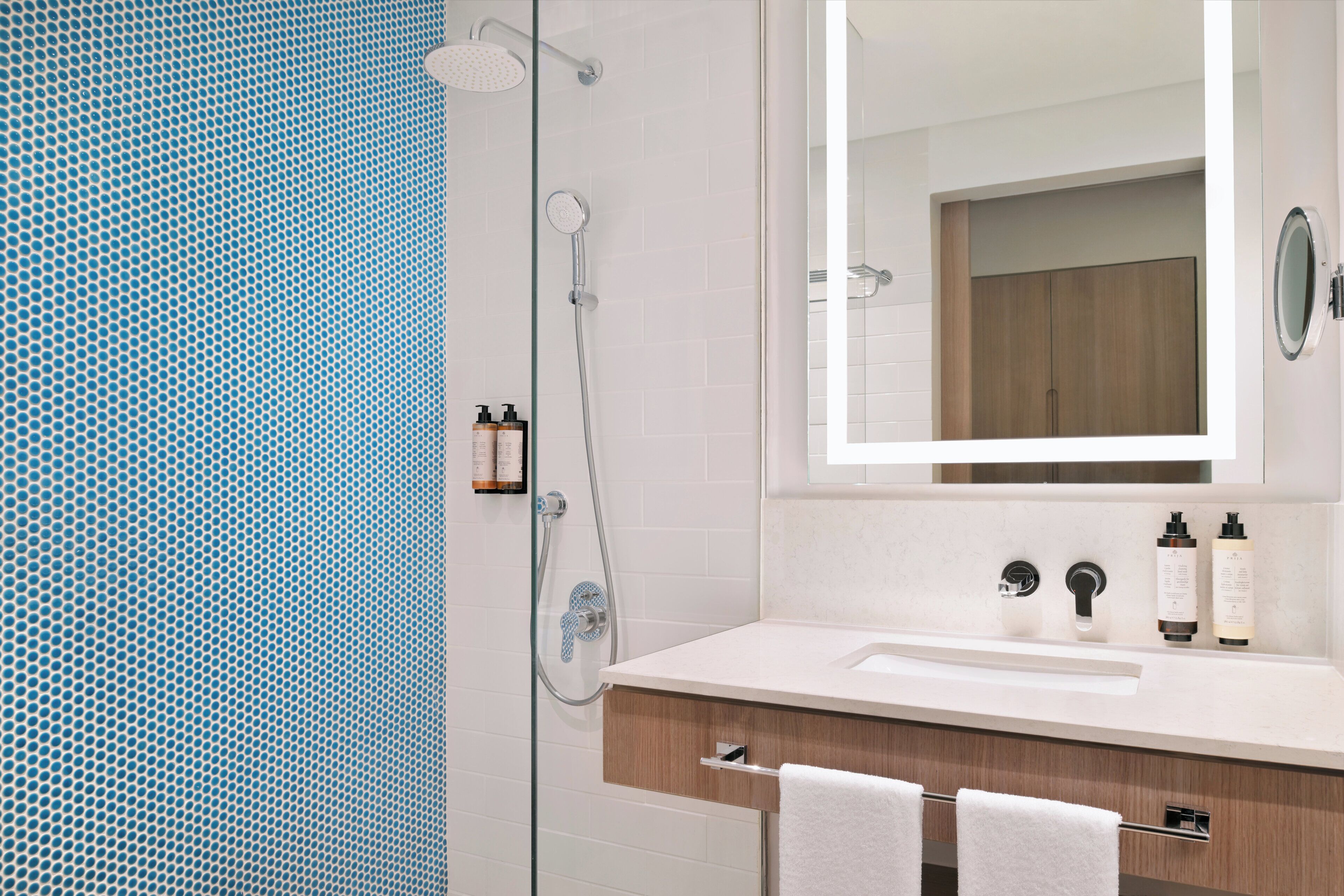 A modern bathroom with a glass shower enclosure, a white sink with a wooden vanity, and a mirror above the sink.
