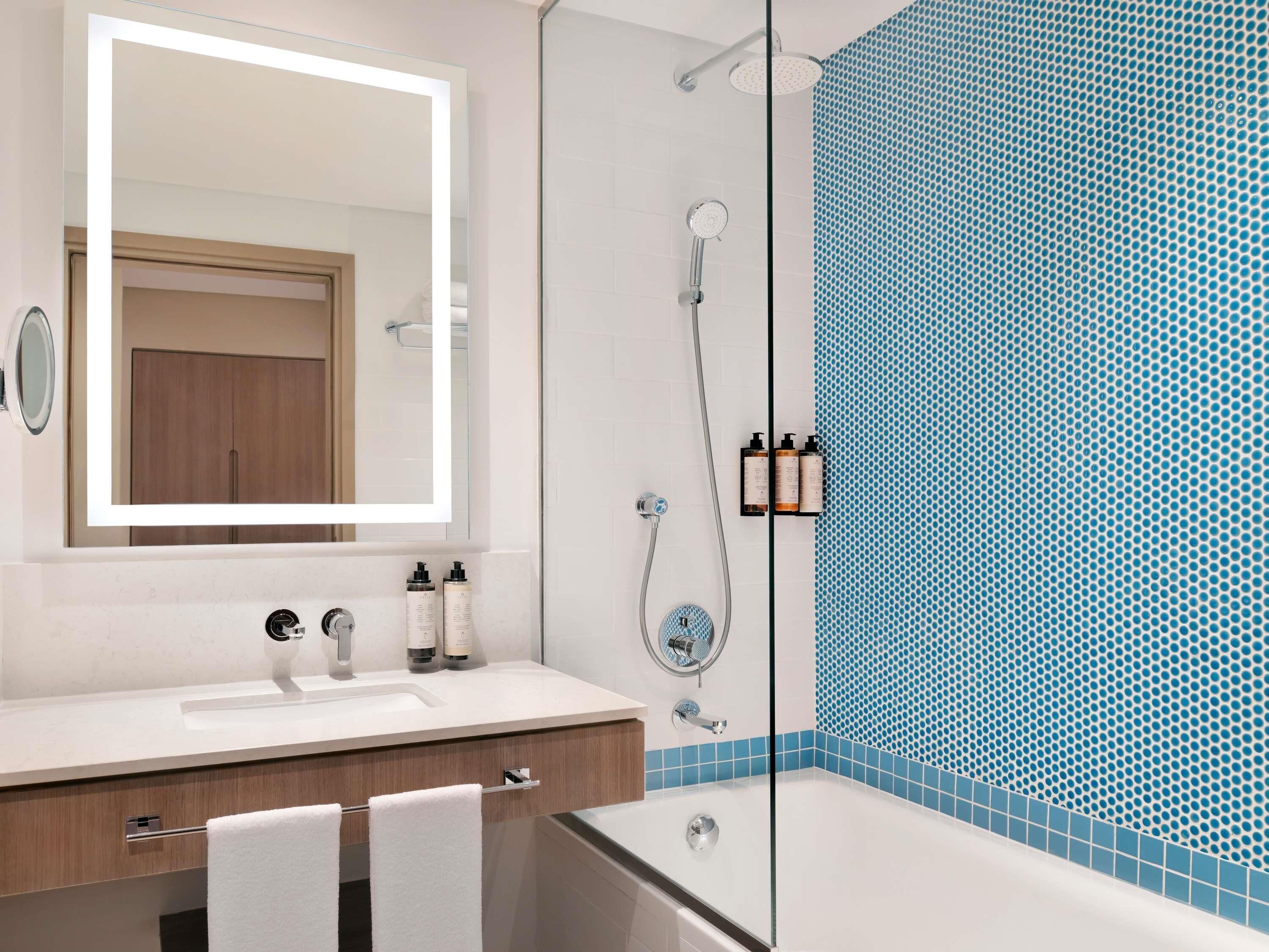 A bathroom with a white sink, mirror, and shower. There are two bottles on the sink and a towel rack.