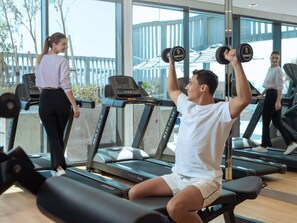 Un gimnasio con cintas de correr, máquinas de pesas y una persona levantando mancuernas.