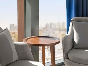 Una habitación moderna con vistas a un horizonte urbano a través de grandes ventanales, una mesa redonda de madera y dos sillas tapizadas en gris.