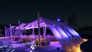 Un área de comedor al aire libre con mesas y sillas bajo una estructura similar a una carpa.