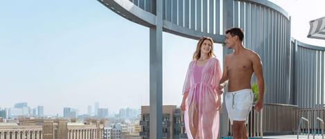 A rooftop pool area with a view of the city skyline, a curved railing, and a clear sky.