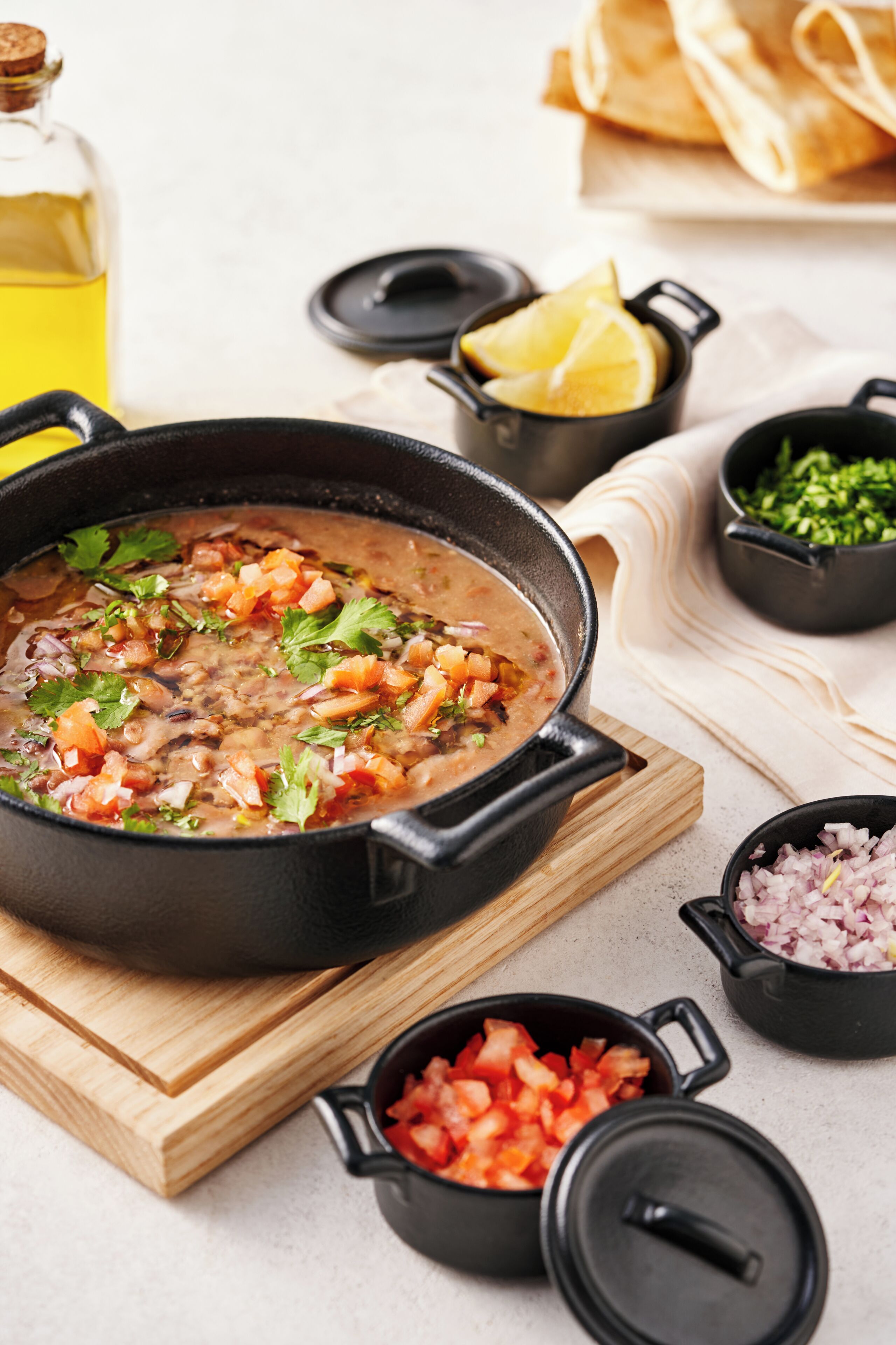 A cooking pot with a stew on a wooden board, surrounded by ingredients and utensils.