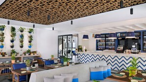 A modern cafe with wooden ceiling, blue and white chevron wall design, and multiple seating areas with tables and chairs. - Mercure Dubai Deira (Dubai)