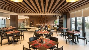 A modern dining area with multiple tables and chairs, wooden ceiling panels, and pendant lighting. - Mercure Tirana (Tirana)