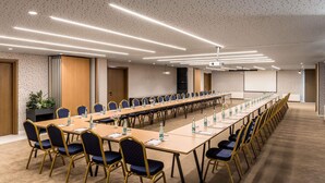 A conference room with a long table, chairs, a projector screen, and a carpeted floor. - Mercure Tirana (Tirana)