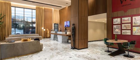 A modern hotel lobby with a reception desk, seating area, and artwork on the walls.