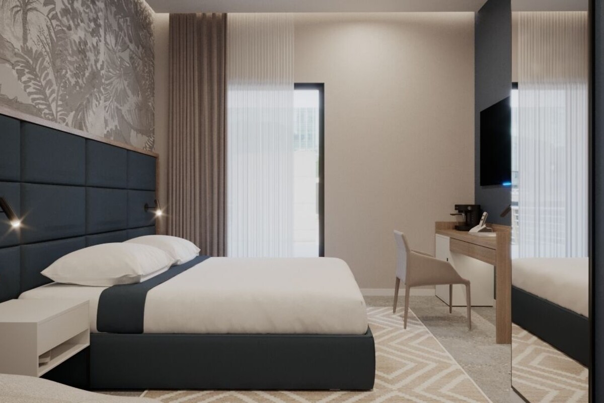 A modern hotel room with a large bed, a desk, a chair, and a television.