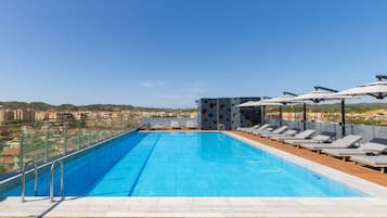 A rooftop swimming pool with lounge chairs and umbrellas, surrounded by a cityscape view.