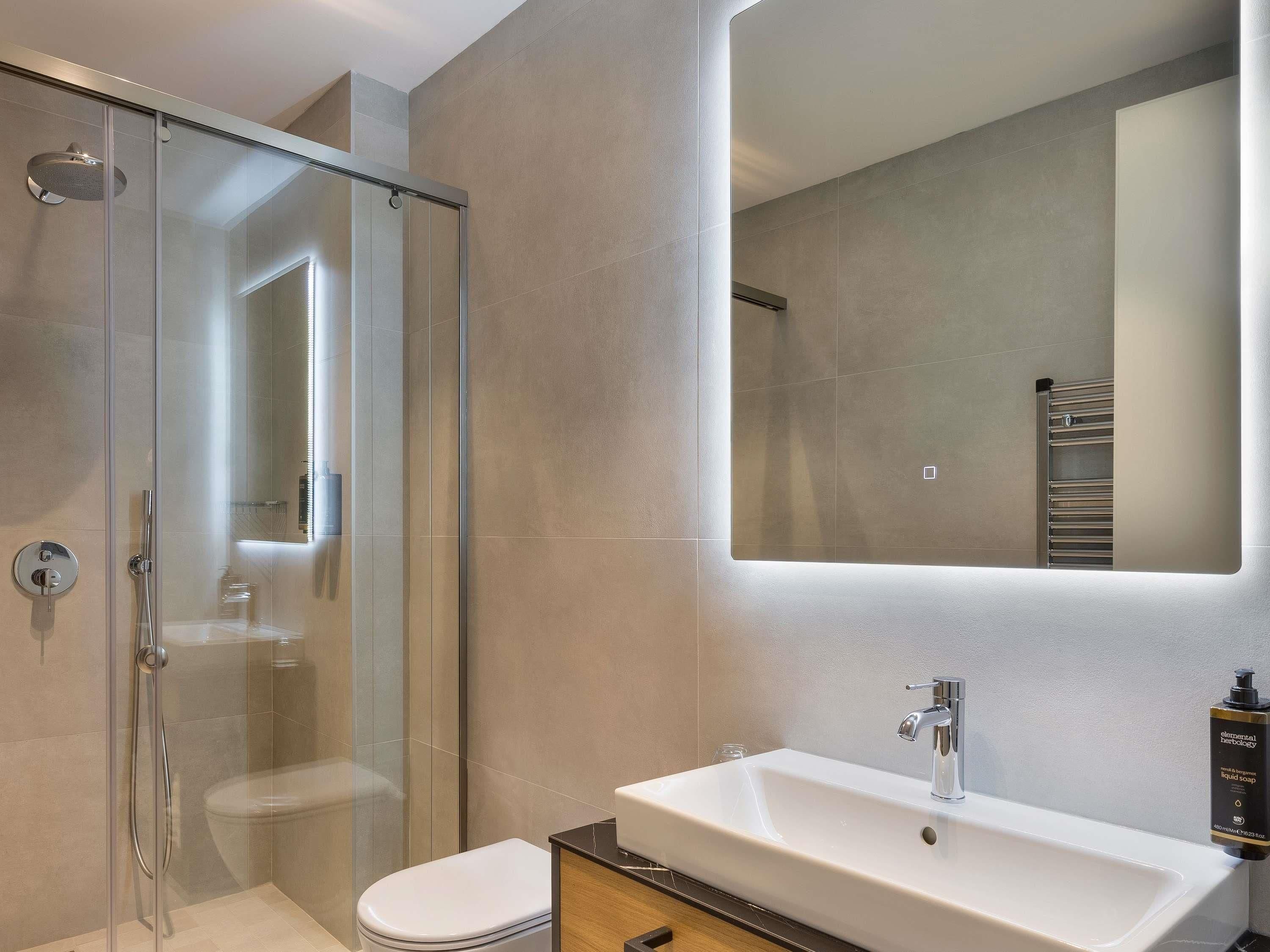 A modern bathroom with a glass-enclosed shower, a white sink, and a large mirror.