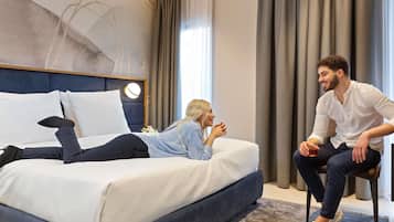 Habitación de hotel moderna con una cama grande, una mesita de noche con lámpara y vistas al exterior a través de una ventana con cortinas.