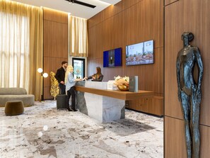 Zona de recepción de un hotel con suelo de mármol, paneles de madera, un mostrador de recepción y una estatua.