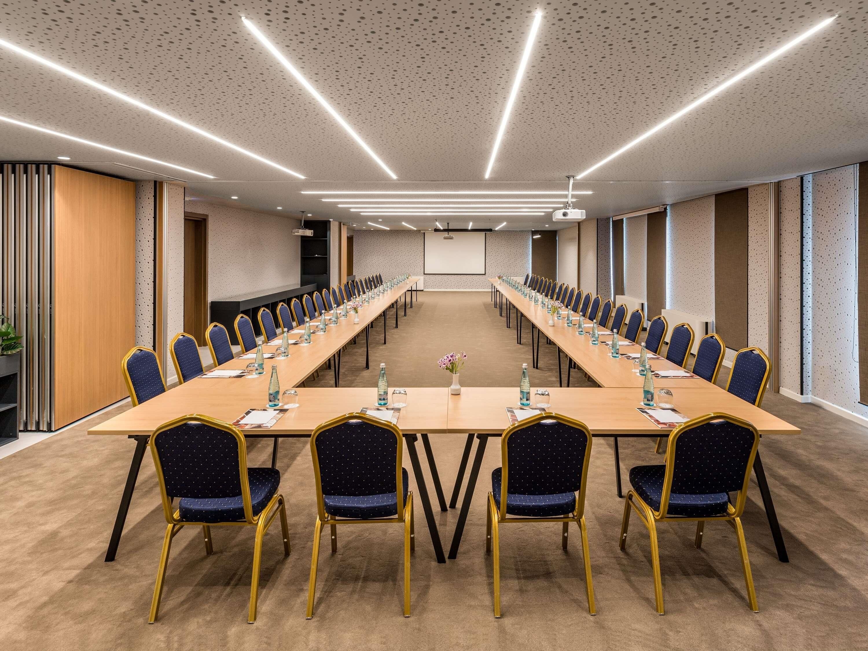Un salón de conferencias con una larga mesa, sillas y una pantalla para proyector.