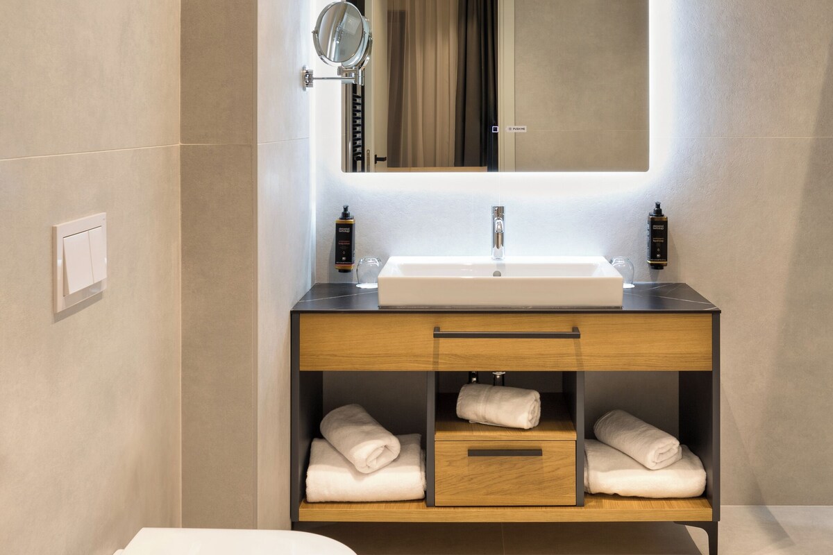 A modern bathroom with a white toilet, a sink with a mirror above it, and a shelf with towels.