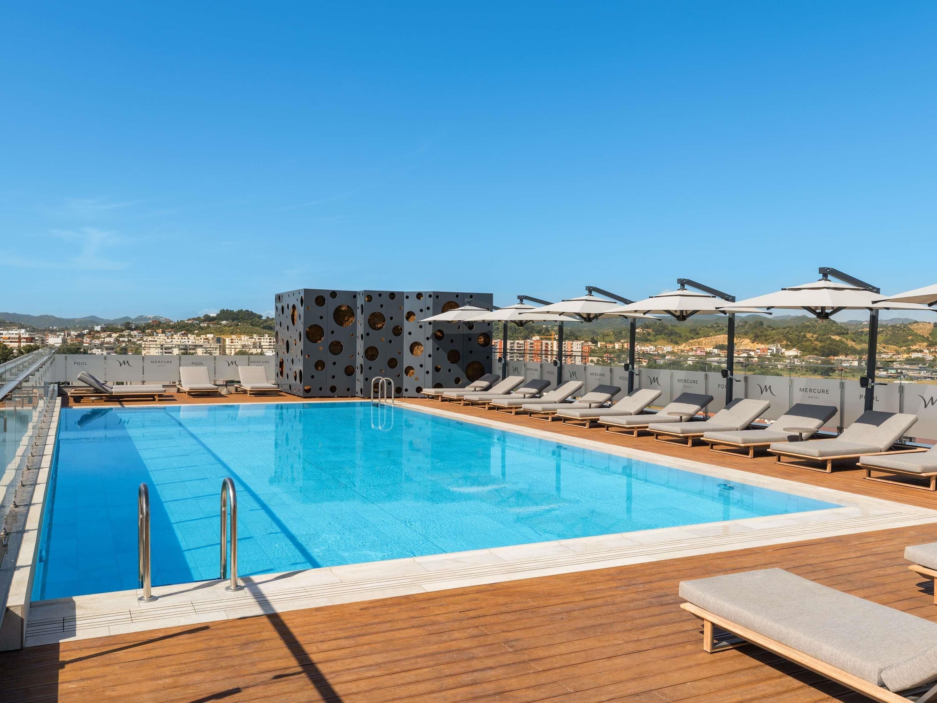 Una piscina en la azotea con sillones y sombrillas, con vistas a un paisaje urbano.