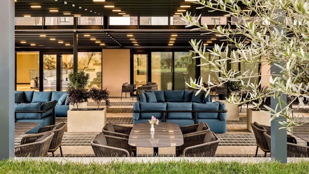 An outdoor seating area with blue sofas and wicker chairs, a marble table, and a view of a modern building with large windows. - Mercure Tirana (Tirana)