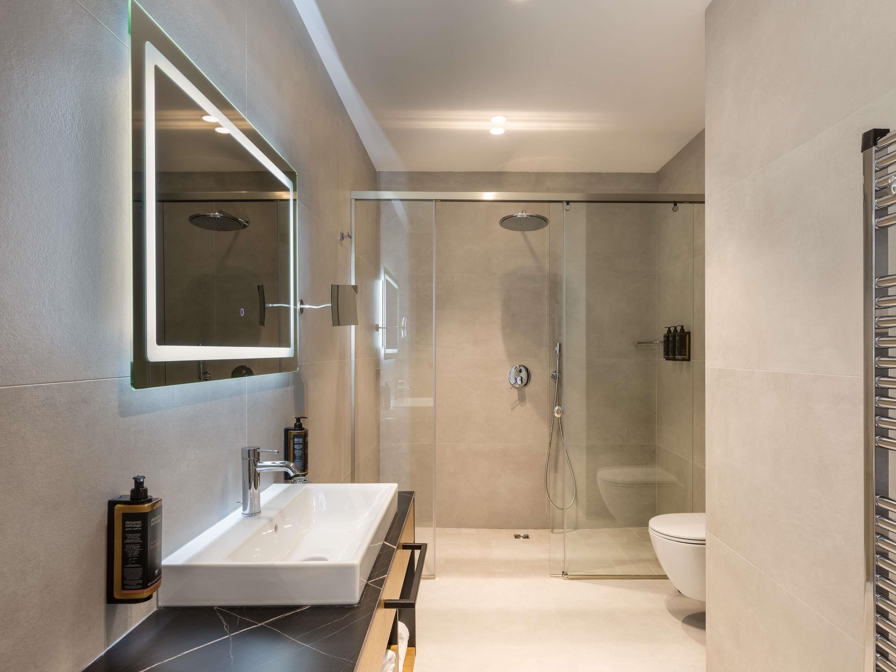 A modern bathroom with a glass-enclosed shower, a large mirror, and a white sink.