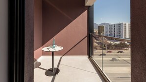 A balcony with a round table and a bottle, overlooking a parking lot and buildings. - Mercure Tirana (Tirana)