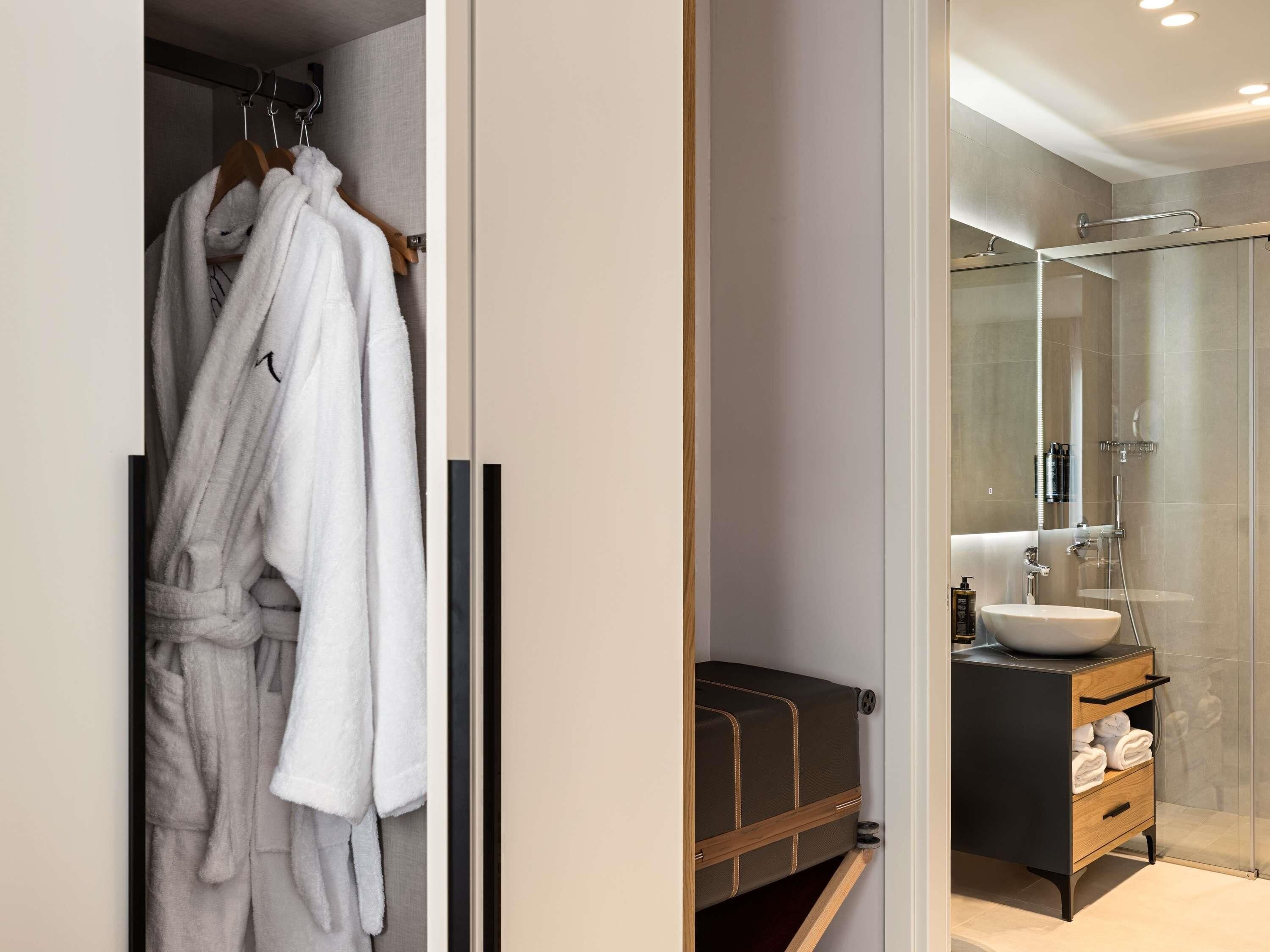 A modern bathroom with a glass shower enclosure, a wooden vanity, and a robe rack with white robes.