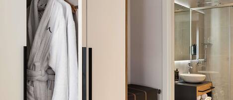 A modern bathroom with a glass shower enclosure, a wooden vanity, and a robe rack with white robes.