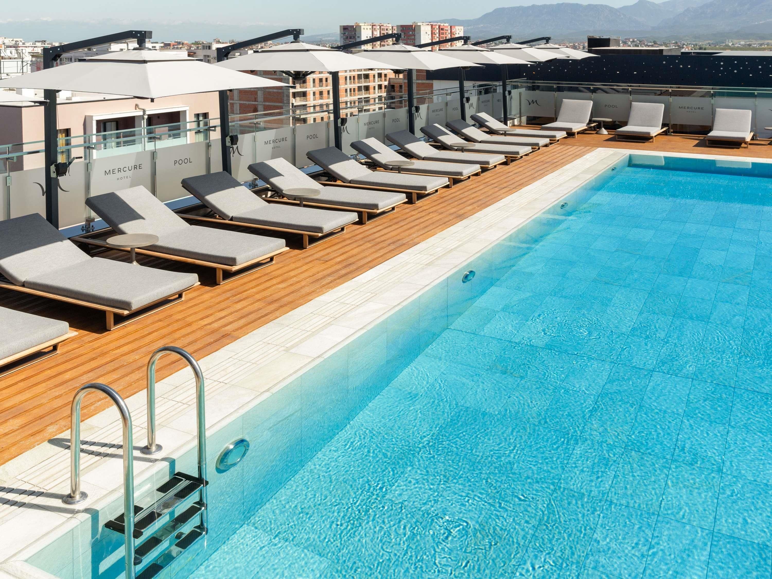 Piscina no terraço com espreguiçadeiras e guarda-sóis, piscina azul cristalina e vista panorâmica da cidade.
