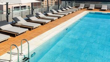 Piscina no terraço com espreguiçadeiras e guarda-sóis, piscina azul cristalina e vista panorâmica da cidade.