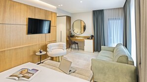 A modern hotel room with a flat-screen TV, a round mirror, a desk, a comfortable sofa, and a laptop on the bed. - Mercure Tirana (Tirana)