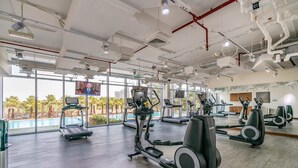 A gym with treadmills, elliptical machines, and a large mirror wall. - Silkhaus Balcony With Great View Studio In Difc (Dubai)