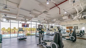 Une salle de sport équipée de matériel d’exercice, dotée de grandes fenêtres et offrant une vue sur des palmiers.