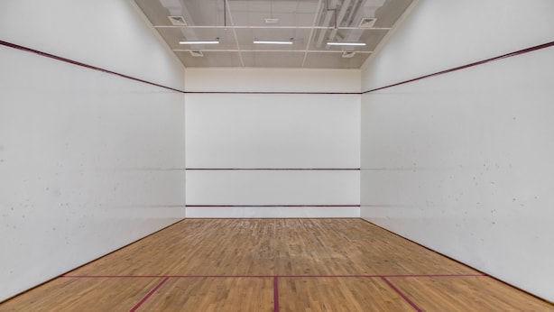 Un court de squash doté d’un plancher en bois et de murs blancs.