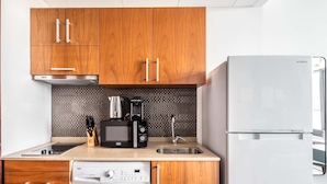 Une cuisine compacte dotée de meubles en bois, d’un lave-linge, d’un four à micro-ondes, d’une machine à café et d’un réfrigérateur Samsung.