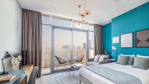 Une chambre d’hôtel moderne dotée d’un grand lit, d’un bureau, d’une chaise, d’un balcon avec vue sur la ville et d’un mur d’accent bleu.