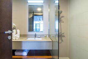 A modern bathroom with a glass shower enclosure, a sink with a mirror above it, and neatly folded towels on the counter. - Silkhaus Modern Studio in Difc Iconic Tower (Dubai)