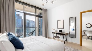 Une chambre d’hôtel moderne dotée d’un grand lit, d’un bureau et offrant une vue sur le paysage urbain grâce à de grandes fenêtres du sol au plafond.