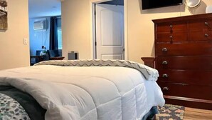 A hotel room with a large bed, a wooden dresser, a flat-screen TV mounted on the wall, and a door leading to another room. - Walla Walla Downtown Getaway (Walla Walla)