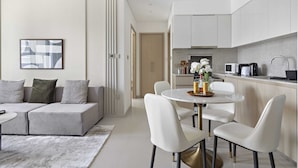 A modern living room with a grey sofa, a round dining table with white chairs, and a kitchen area with white cabinets and appliances. - Silkhaus Elegant Downtown Premium Tower w Pool (Dubai)