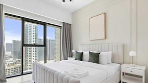A modern hotel room with a large bed, a nightstand, a bedside table, and a view of the cityscape through floor-to-ceiling windows. - Silkhaus Elegant Downtown Premium Tower w Pool (Dubai)