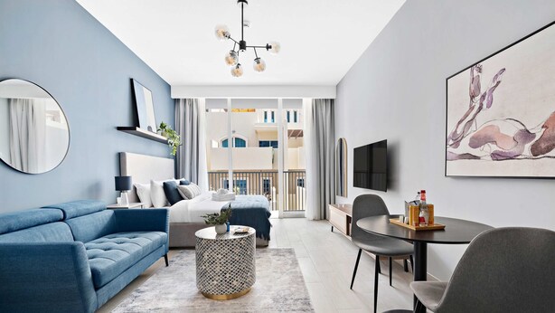 A modern living room with a blue sofa, a round coffee table, and a dining area with a table and chairs. - Silkhaus New Large Furnished Studio in Luma21 (Dubai)