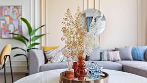 Un salon moderne avec une table basse ronde, un vase contenant des branches séchées, une bougie et une sphère de verre décorative.