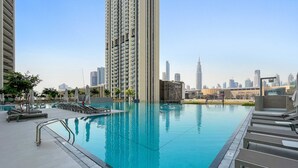 En pool på taget med liggestole, en bysilhouet i baggrunden og en moderne bygning med 'EMAAR'-skiltning.