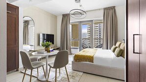 Una moderna camera d'albergo con un letto grande, un'area pranzo con due sedie, una televisione e un balcone con tende.