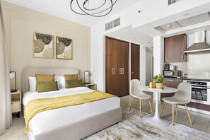 Ein modernes Hotelzimmer mit einem großen Bett, Nachttischen, einem kleinen Esstisch und einer Küchenzeile.