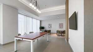 Ein modernes, helles Zimmer mit einem langen Holztisch, einer Zimmerpflanze und einem flachbildfernseher an der Wand.