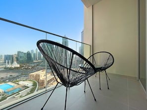 A balcony with two black wireframe chairs, a city view, and a swimming pool in the background. - Silkhaus Opera District in Downtown New Tower (Dubai)