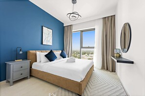 Quarto com cama grande, mesa de cabeceira, prateleira na parede, luminária no teto, janela com cortinas e vista para a cidade.