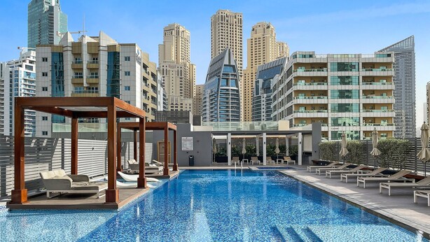A rooftop pool with lounge chairs and a wooden pergola, surrounded by high-rise buildings. - Silkhaus Luxurious Studio in Studio One Tower (Dubai)