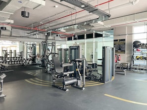 A modern gym with various exercise machines, a mirrored wall, and a well-lit space with visible ceiling pipes and ventilation. - Silkhaus Luxurious Studio in Studio One Tower (Dubai)
